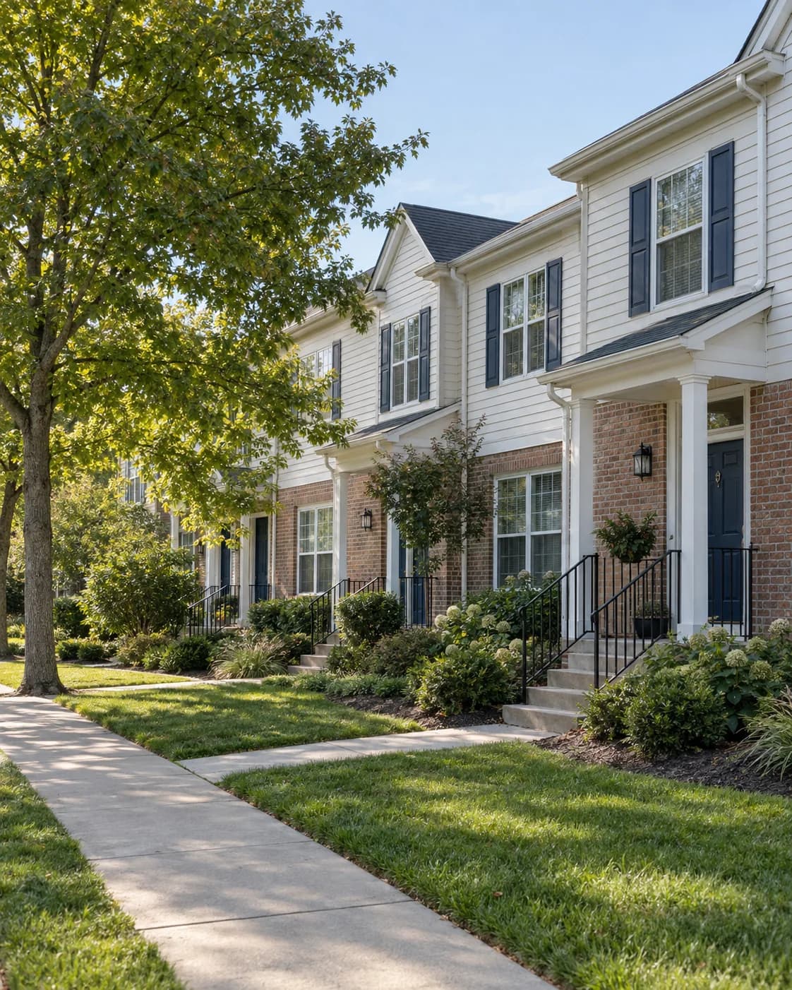 Brick and white-sided US townhomes with shared sidewalks, front porches, and landscaped grounds